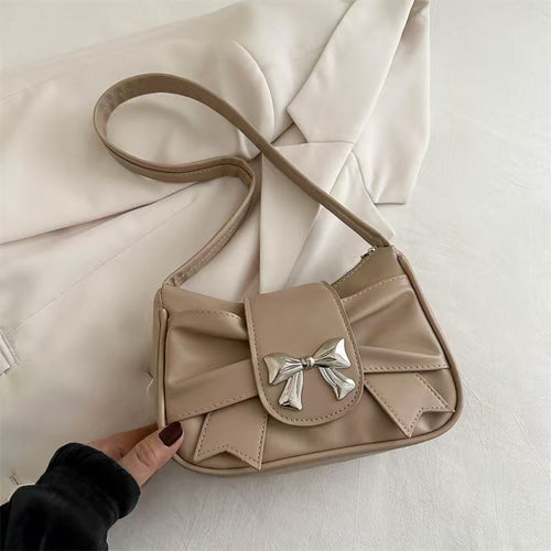 Beige handbag with a bow detail held by a hand on a light background