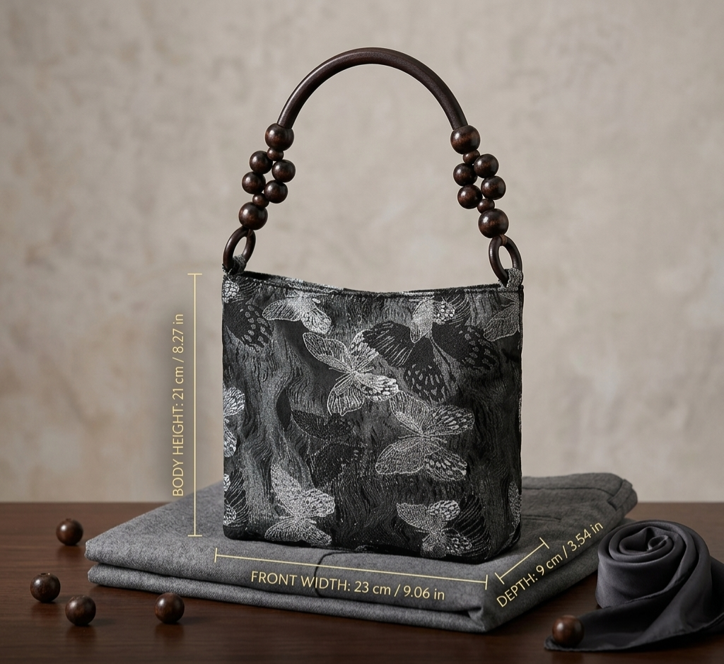 A black and gray butterfly-patterned handbag with dark brown wooden bead handles, displayed on a gray fabric cushion with dimension overlays showing its height, width, and depth.